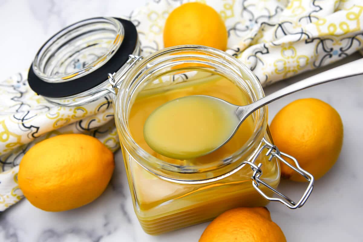 A top view of a glass jar filled with egg-free lemon curd with lemons on the side.