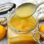 A close up of a spoonful of vegan lemon curd above a glass jar.