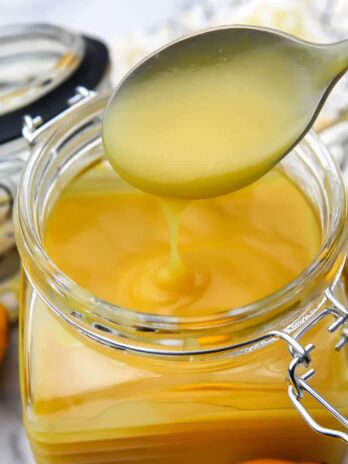 A close up of a spoonful of vegan lemon curd above a glass jar.