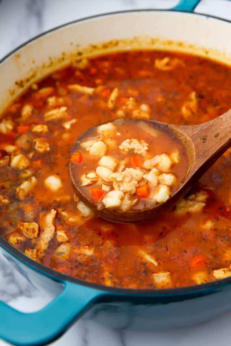 A large blue pot filled with vegan posole with some being scooped out with a wooden ladel.