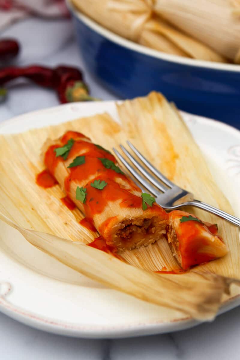 A vegan tamale on a plate still on top of the unwrapped corn husk.