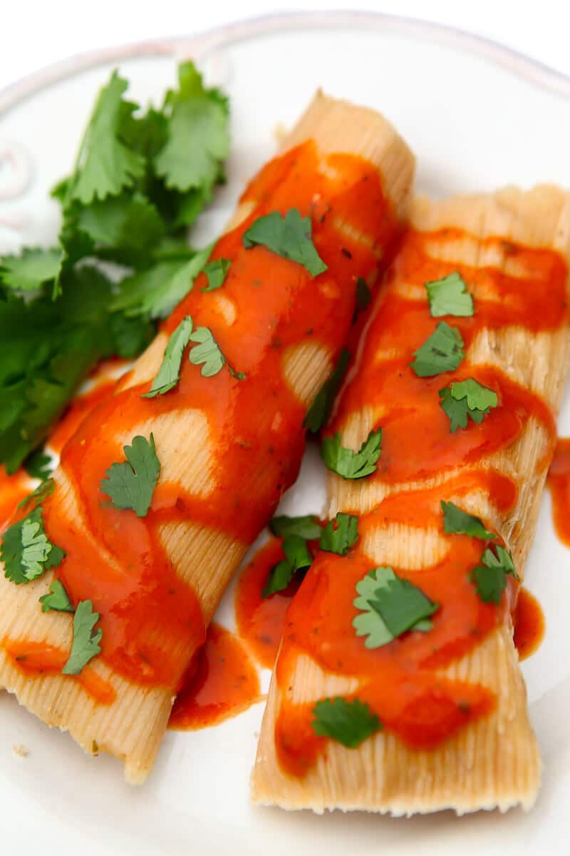 Two tamales covered in New Mexico red chile sauce and garnished with cilantro.