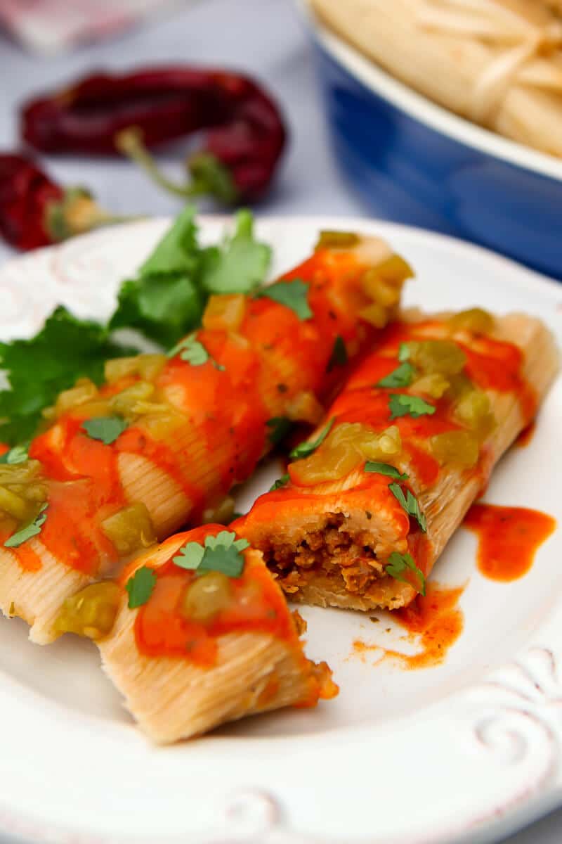Two vegan tamales on a white plate covered in red and green chile sauce.
