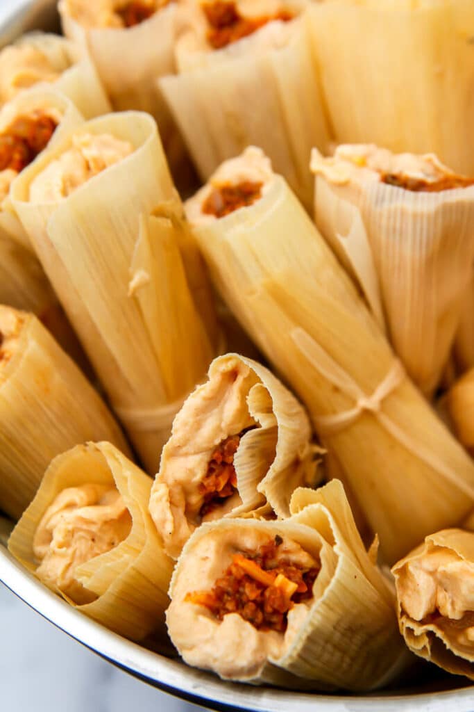 A steamer pot filled with vegan tamales wrapped in corn husks.