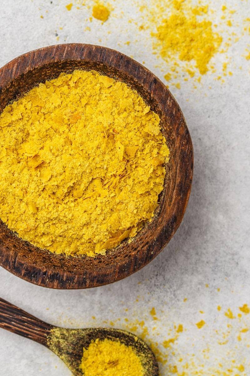 A wooden bowl filled with yellow nutritional yeast flakes.