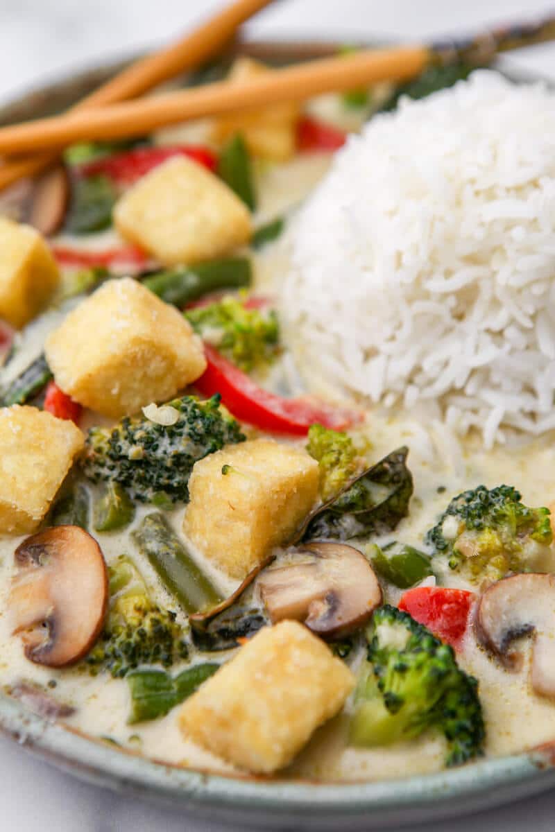 A close up of green coconut curry with crispy tofu and veggies served with rice.