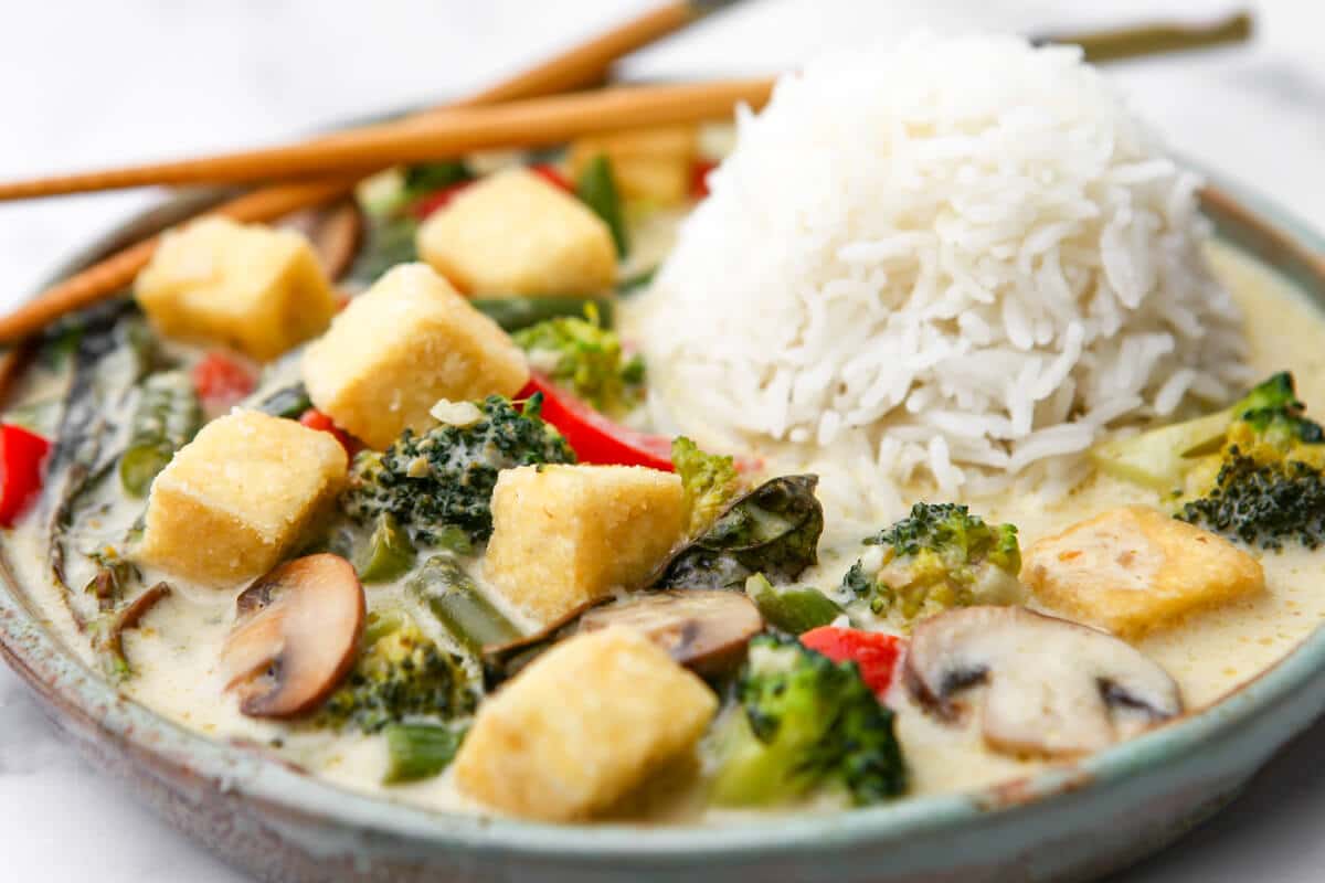 A plate full of veggie green curry with tofu served with white rice.