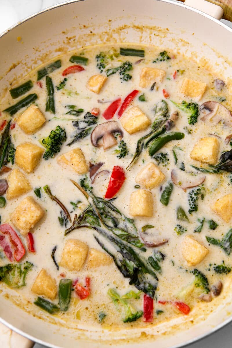 A large wok filled with Thai green curry with veggies, coconut milk, and tofu.