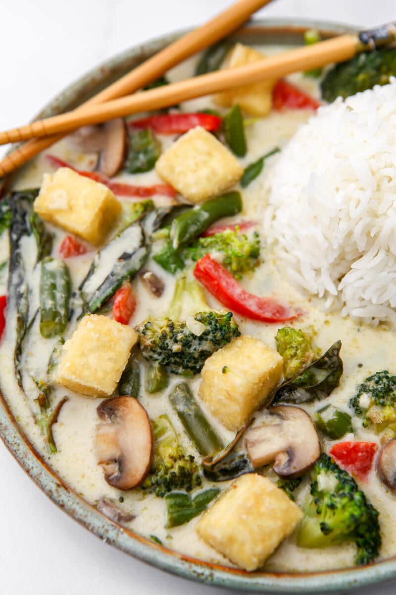 A top view of a vegan coconut green curry with vegetables and rice.