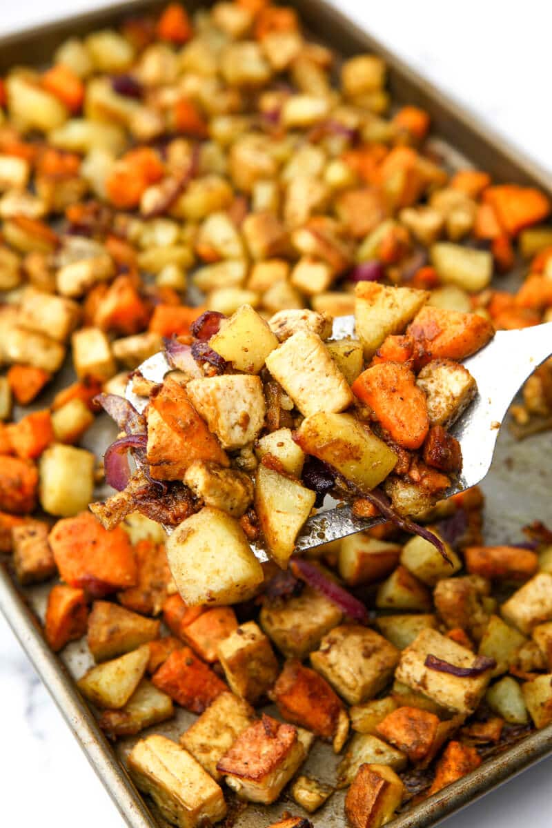 A spatula full of roasted root veggies held above a sheet pan.
