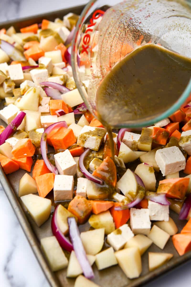 A sheet pan filled with root vegetables being drizzled with a savory dressing before baking.
