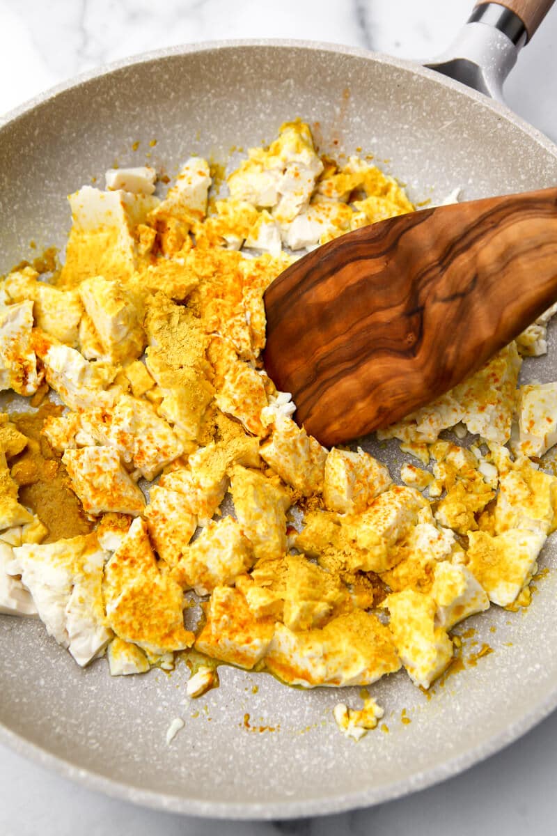 A frying pan filled with crumbled silken tofu and spices sprinkled over top of it.