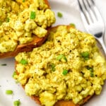 A silken tofu scramble on top of a bagel with a fork on the side.