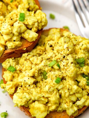 A silken tofu scramble on top of a bagel with a fork on the side.