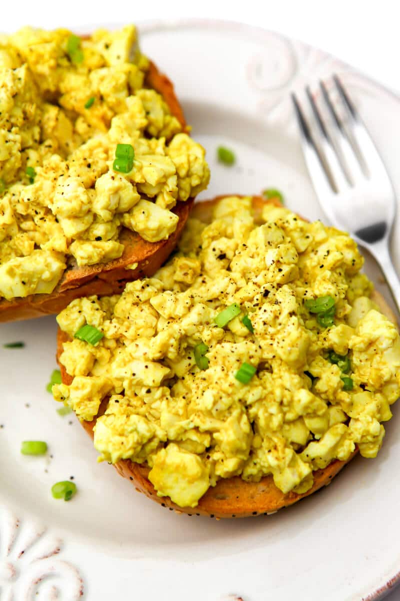 Two halfs of a bagel with a tofu scramble made with silken tofu on top and sprinkled with pieces of green onions.