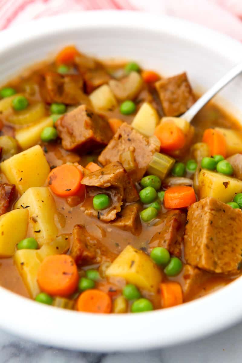A white bowl filled with vegan beef stew with potatoes, carrots, peas, and vegan beef.