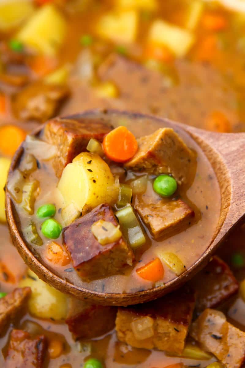 A close up of a pot a vegan beef stew being scooped with a wooden ladel.