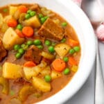 A white bowl filled with vegan beef stew with potatoes, carrots, peas and vegan beef.