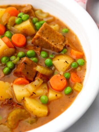 A white bowl filled with vegan beef stew with potatoes, carrots, peas and vegan beef.