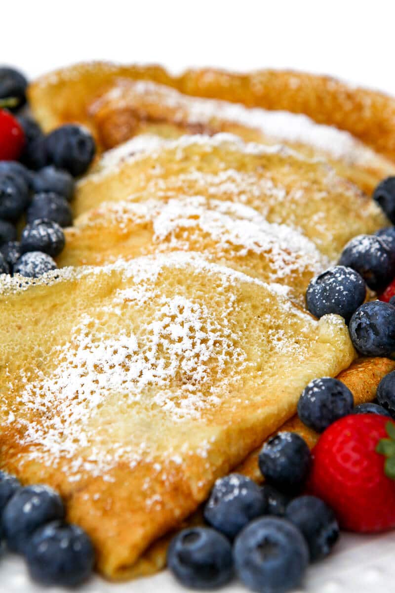 A close-up of egg-free chickpea crepes dusted with powdered sugar with berries on the side.