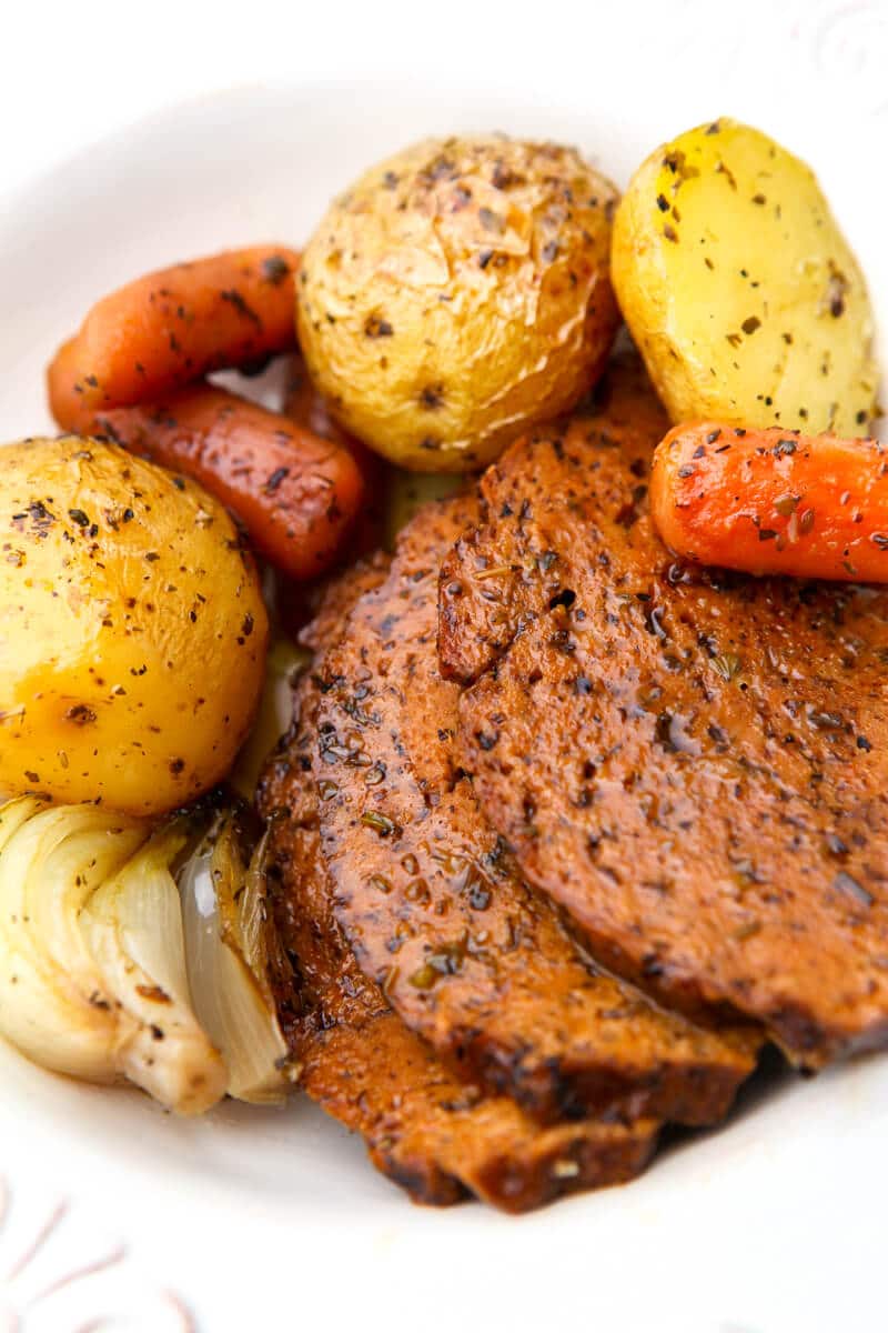 Slices of vegan pot roast with potatoes and carrots on the side on a white plate.