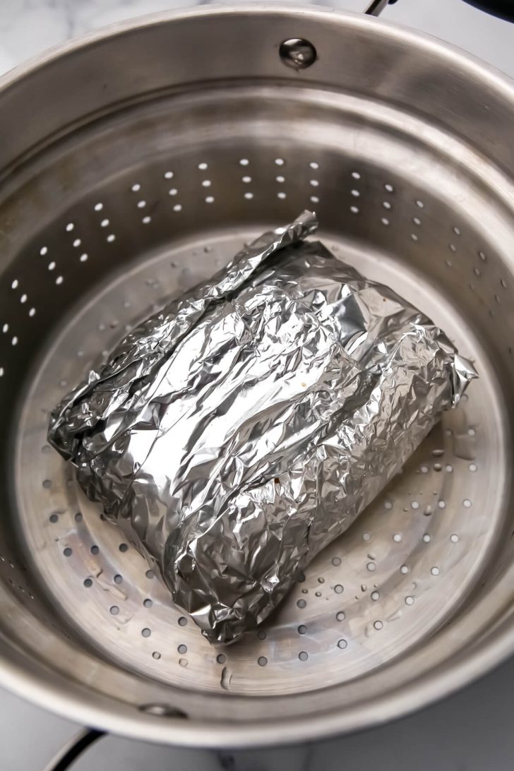 The seitan wrapped in foil in a steamer basket.
