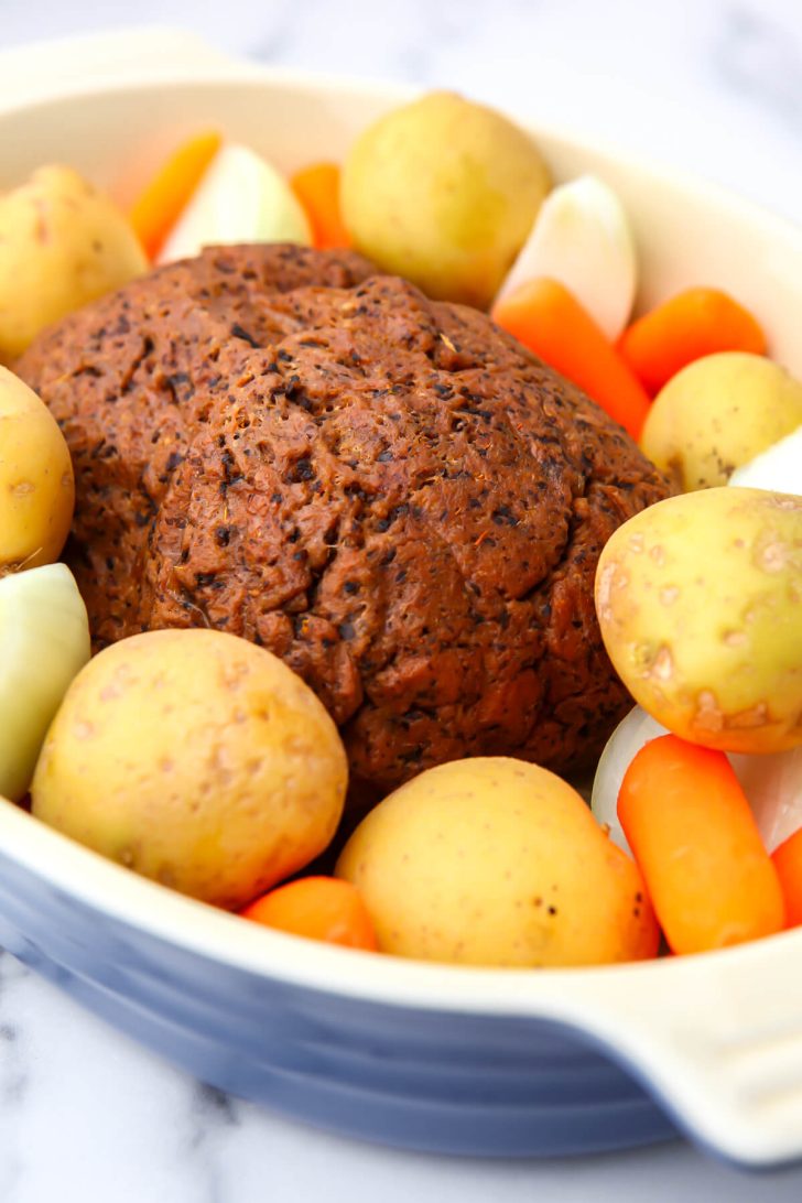 Beef seitan roast surrounded by potatoes, carrots and onions in a baking dish.