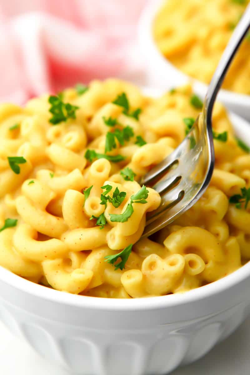 A fork in a bowl of vegan mac and cheese with parsley sprinkled on top.