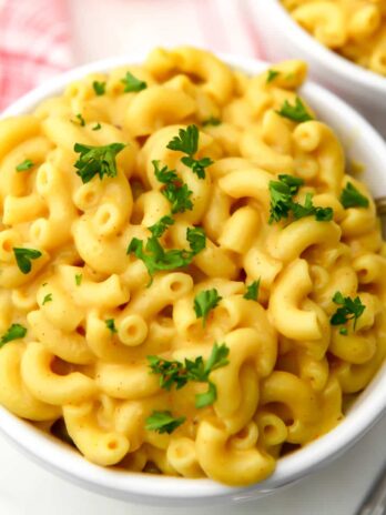 A top view of a bowl of coconut milk mac and cheese with parsley sprinkled on top and a fork in the bowl.