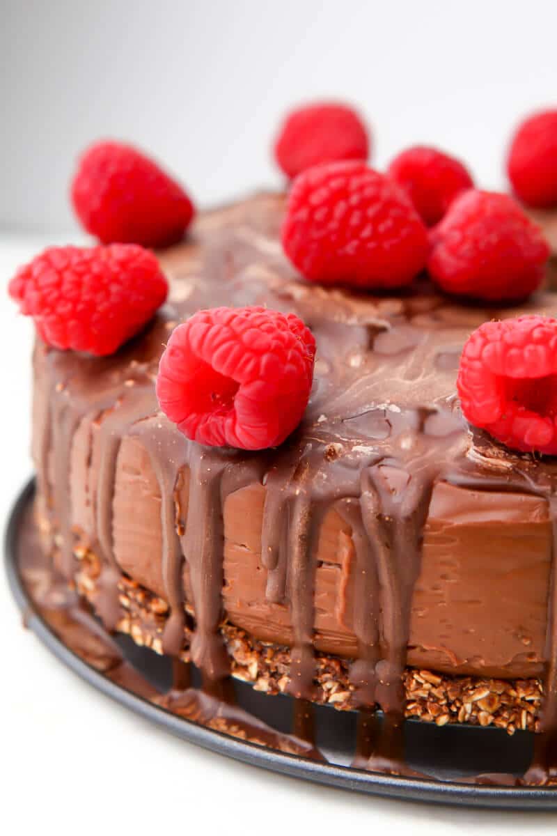 A vegan chocolate cheesecake with a chocolate drizzle and raspberries on top.