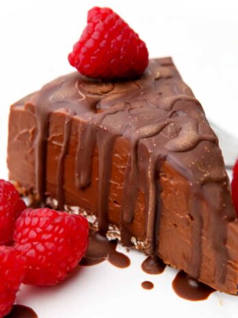 A slice of vegan chocoalte cheesecake with a gluten-free crumble crust and chocolate and raspberries on top.
