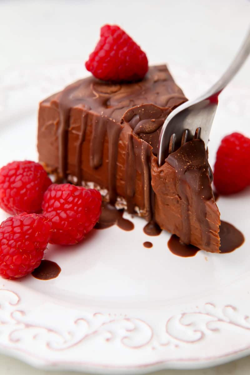 A slice of vegan chocolate cheesecake with raspberries on the side with a fork taking a piece.