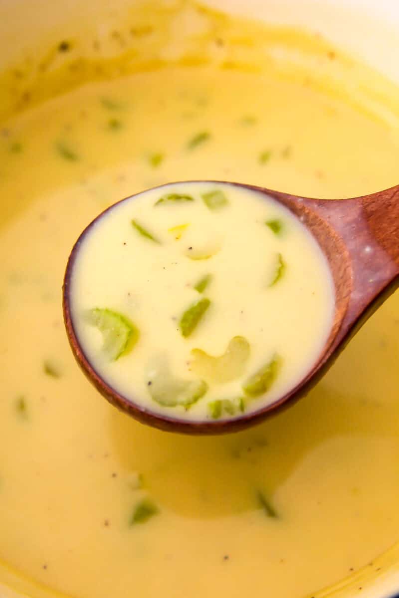 A pot of cream of celery soup being scooped up with a wooden ladel.