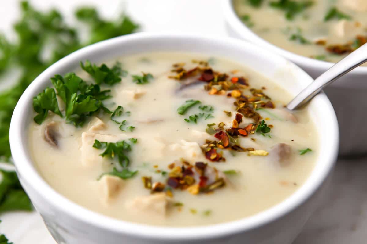  A white bowl of vegan cream of chicken soup with parsley and red and green chili flakes sprinkled on top.