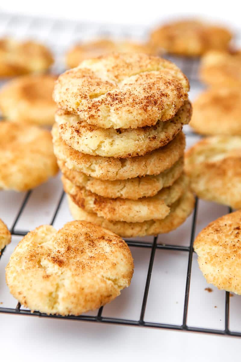 A cooling rack filled with baked vegan snickerdoodles, with a stack of six snickerdoodles in the center.