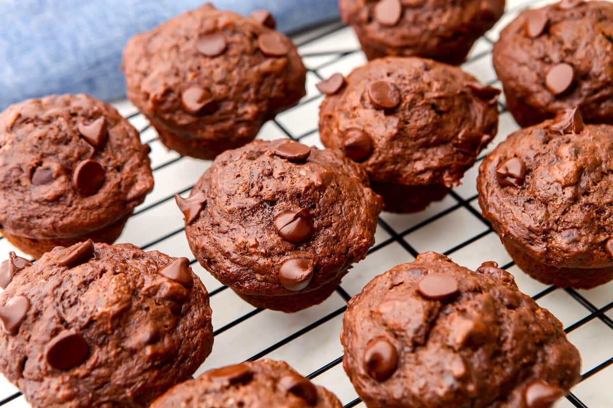 A top view of double chocolate vegan banana muffins on a cooling rack. with a blue tea towel behind them.