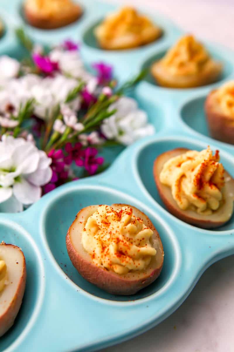 A blue deviled egg plate filled with deviled potatoes and flowers in the middle.
