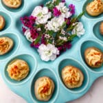 A blue deviled egg plate with vegan deviled potatoes and bright purple flowers in the center.