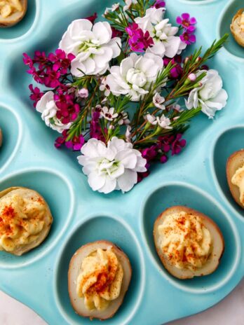 A blue deviled egg plate with vegan deviled potatoes and bright purple flowers in the center.