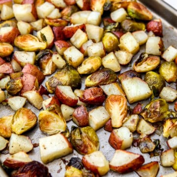 A close up of a roasted potatoes and Brussel sprouts on a sheet pan after baking.