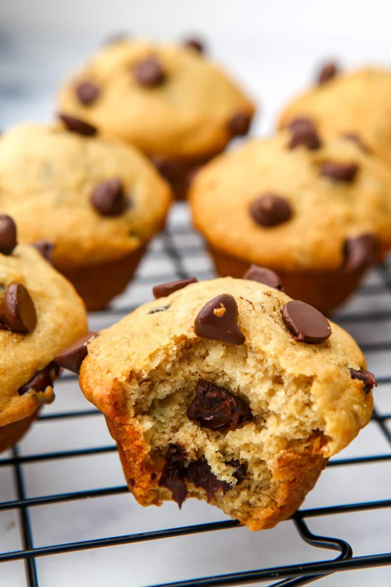 Vegan chocolate chip banana muffins on a cooling rack with a bite taken out of one of them.
