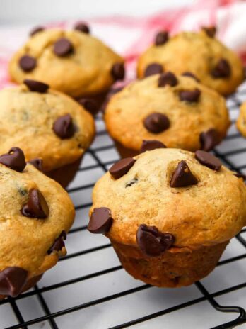 Vegan chocolate chip banana muffins on a cooling wrack with a tea towel behind them.