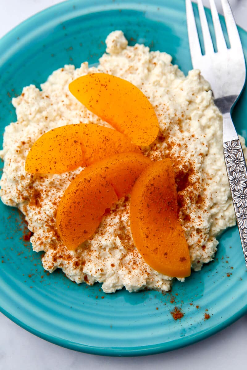 A blue plate with vegan cottage cheese and slice peaches and cinnamon sprinkled on top.