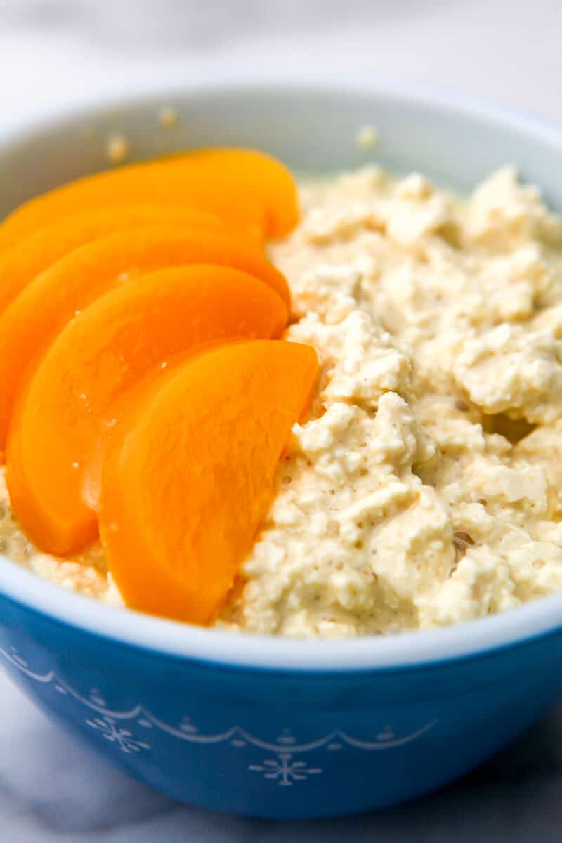 A blue bowl with vegan cottage cheese with peaches on top.