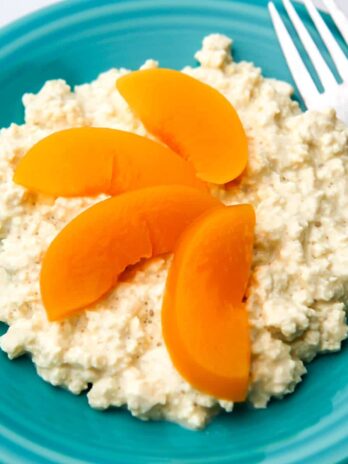 Vegan cottage cheese made from tofu on a blue plate with peach slices on top and a fork on the side.