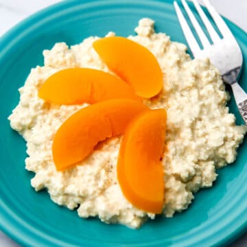 Vegan cottage cheese made from tofu on a blue plate with peach slices on top and a fork on the side.