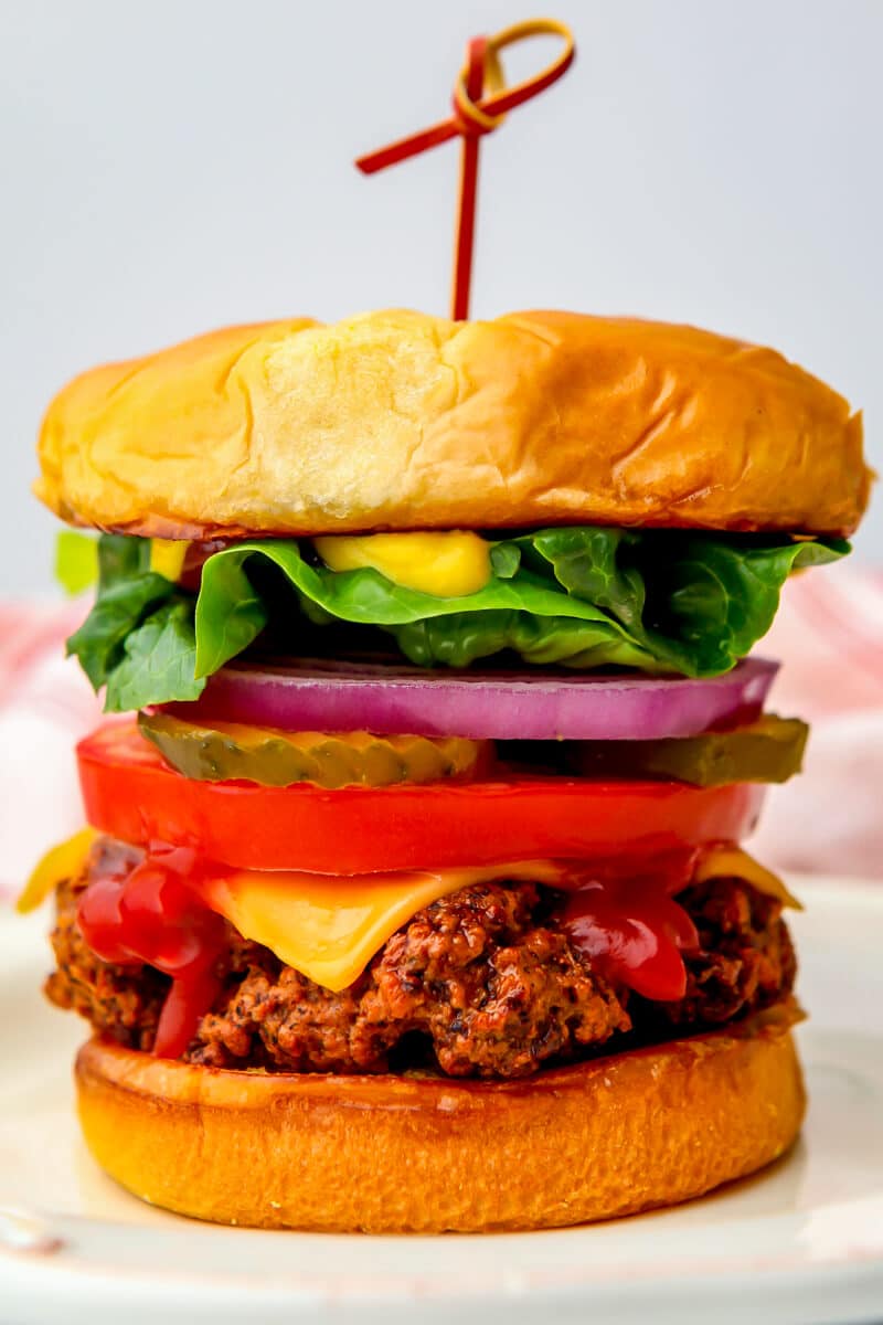 A close up of a veggie burger made from seitan with lettuce, tomatoes, pickles, and red onion.