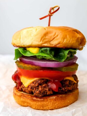 A vegan seitan burger on a toasted bun with lettuce, tomatoes, pickels, red onion, ketchup and mustard on it.