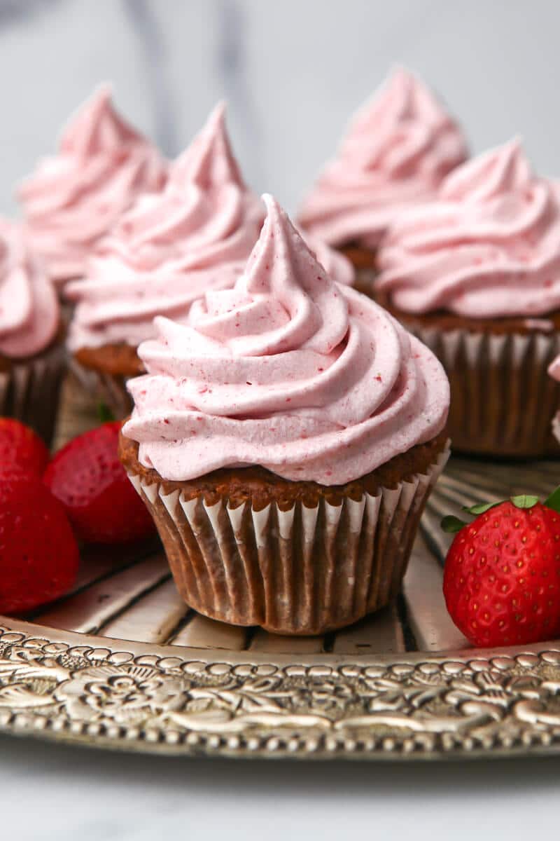 Six vegan strawberry cupcakes on a silver tray topped with vegan stawberry frosting.