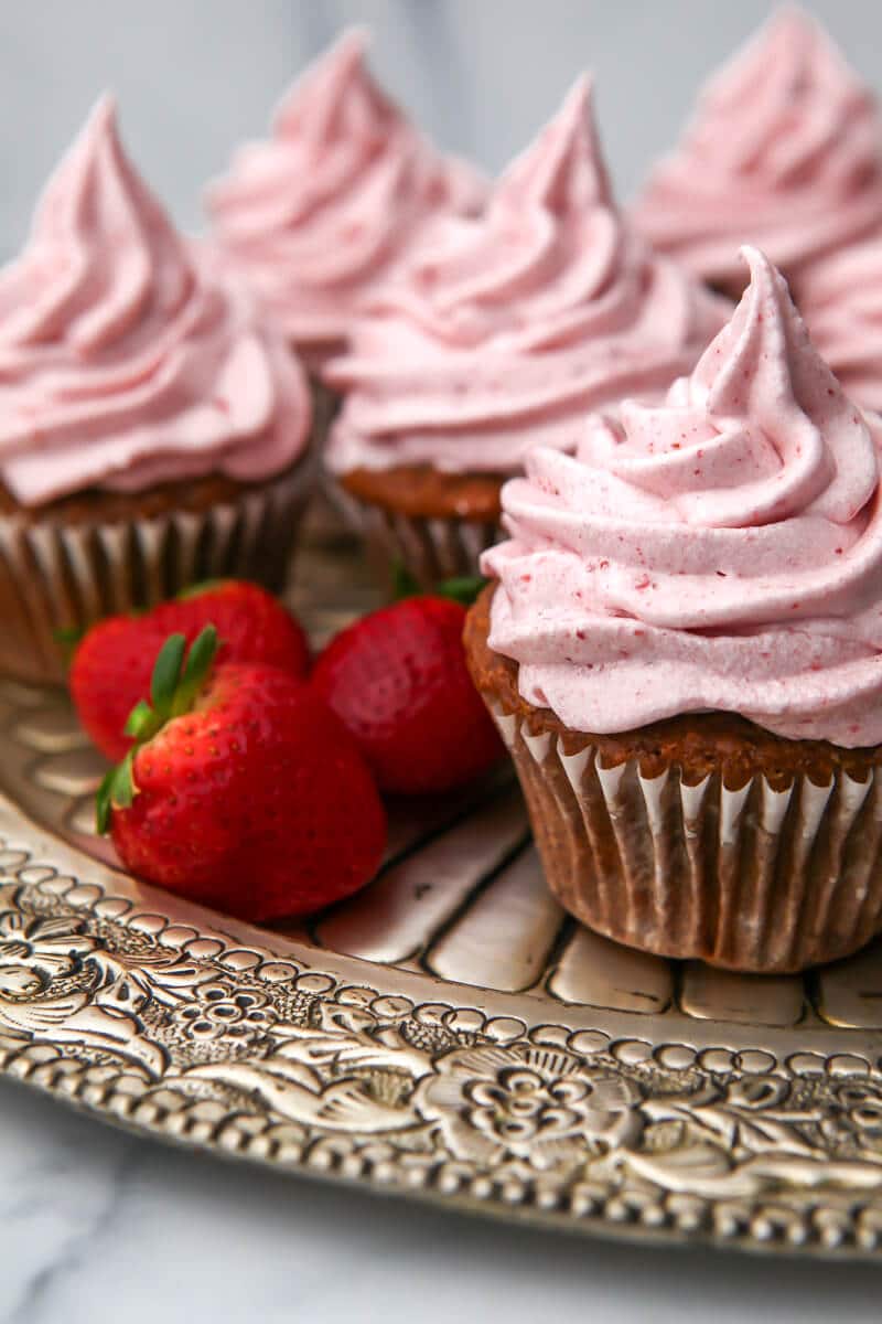 Vegan strawberry cupcakes on a sliver tray with fresh strawberries around them.